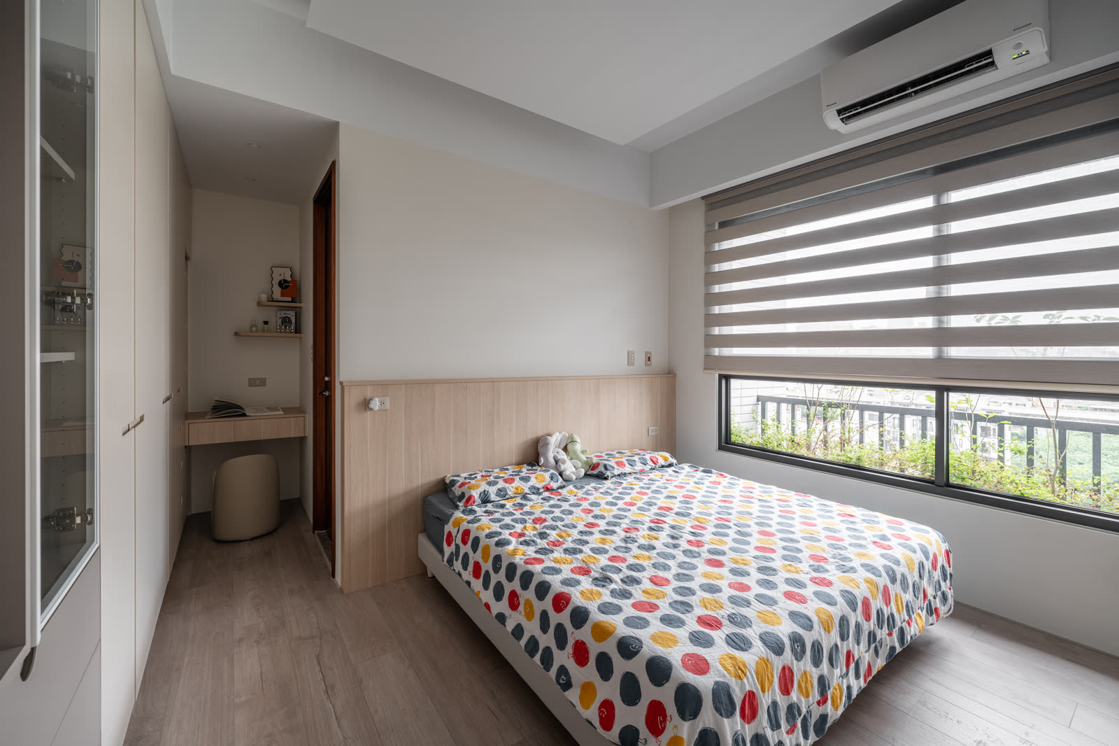 主臥睡眠區完工實景｜雙人床搭配木質床頭矮牆，右側為斑馬簾大面窗景，左側連著梳妝與衣櫃收納區